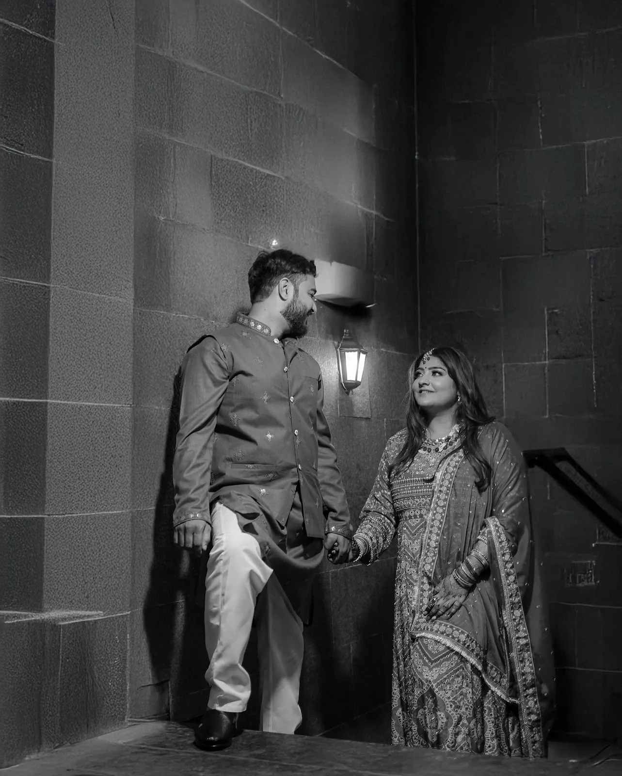 Black and white portrait of a couple holding hands by a stone wall